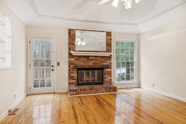 unfurnished living room featuring light wood-type flooring, a tray ceiling, a brick fireplace, and ceiling fan