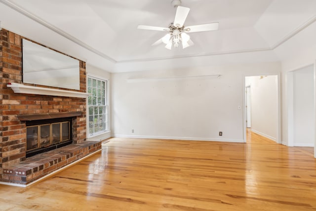 unfurnished living room with a tray ceiling, ceiling fan, a fireplace, and wood-type flooring