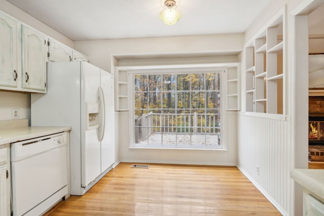 kitchen featuring a brick fireplace, white appliances, wooden walls, light hardwood / wood-style flooring, and white cabinetry