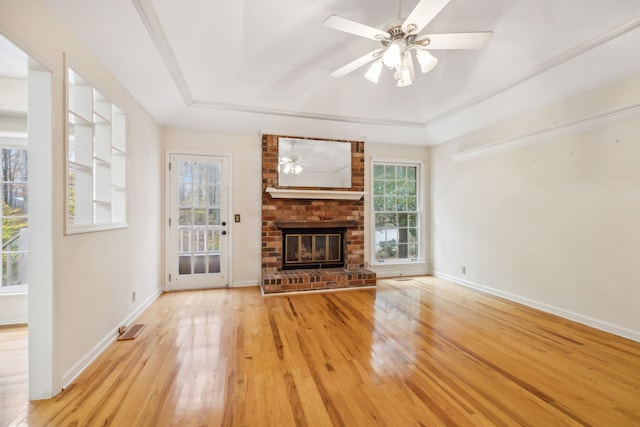 unfurnished living room with light hardwood / wood-style floors, a brick fireplace, a wealth of natural light, and a tray ceiling