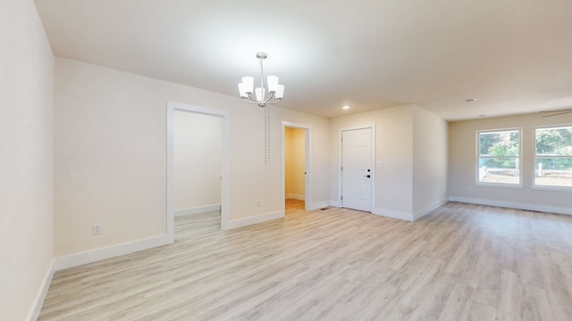 spare room featuring ceiling fan with notable chandelier and light wood-type flooring