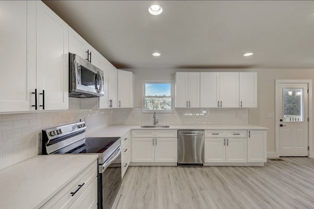 kitchen with white cabinets, sink, decorative backsplash, light wood-type flooring, and stainless steel appliances