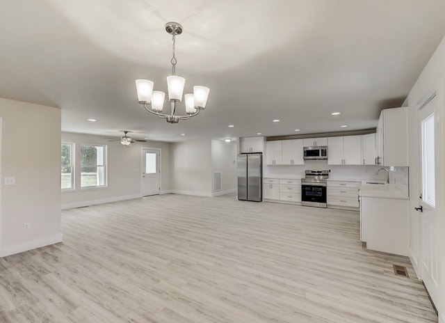 interior space with white cabinetry, sink, stainless steel appliances, decorative light fixtures, and light wood-type flooring