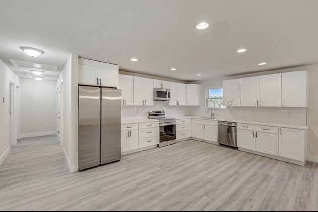 kitchen with sink, backsplash, light hardwood / wood-style floors, white cabinets, and appliances with stainless steel finishes