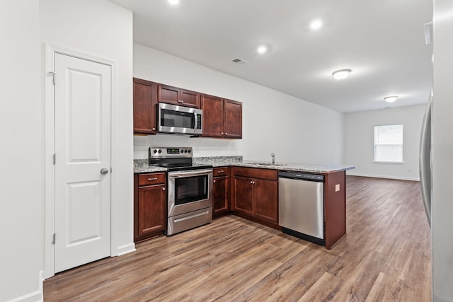 kitchen featuring light stone counters, kitchen peninsula, appliances with stainless steel finishes, and light hardwood / wood-style flooring