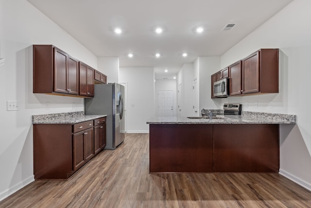 kitchen with kitchen peninsula, light stone counters, dark brown cabinetry, stainless steel appliances, and light hardwood / wood-style flooring