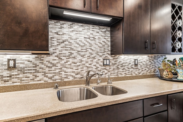 kitchen featuring dark brown cabinetry, backsplash, light stone counters, and sink