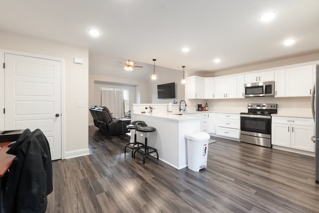 kitchen featuring a breakfast bar, stainless steel appliances, dark wood-type flooring, pendant lighting, and white cabinets