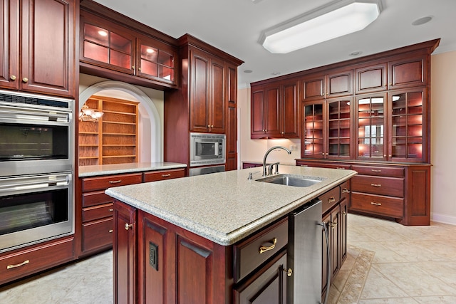 kitchen with light stone counters, stainless steel appliances, sink, light tile patterned floors, and a center island with sink