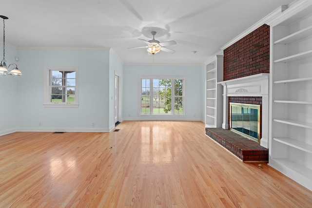 unfurnished living room with ceiling fan with notable chandelier, crown molding, a brick fireplace, built in shelves, and light hardwood / wood-style floors