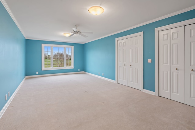 unfurnished bedroom with light carpet, crown molding, ceiling fan, and multiple closets