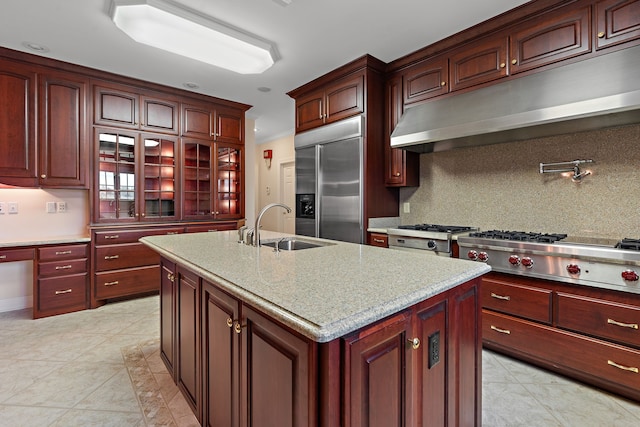 kitchen featuring exhaust hood, a center island with sink, sink, appliances with stainless steel finishes, and light stone counters