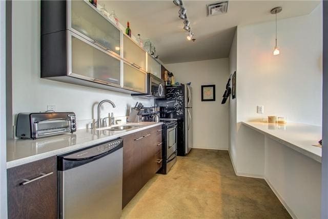 kitchen with track lighting, dark brown cabinets, stainless steel appliances, sink, and hanging light fixtures