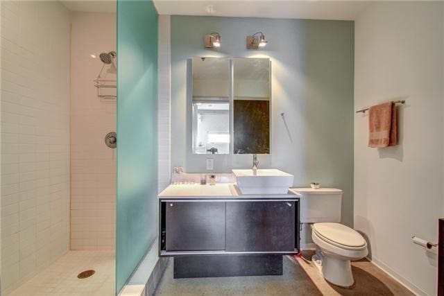 bathroom with a tile shower, vanity, and toilet