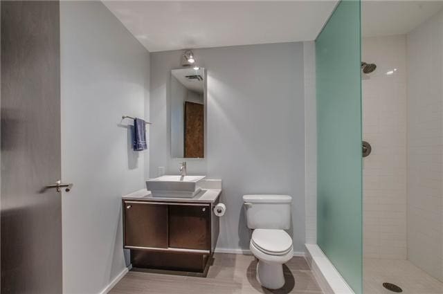 bathroom featuring a tile shower, vanity, hardwood / wood-style flooring, and toilet