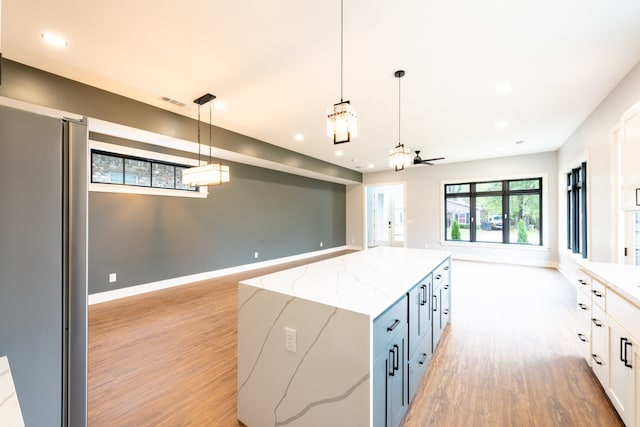 kitchen featuring stainless steel fridge, light stone counters, pendant lighting, light hardwood / wood-style flooring, and white cabinetry