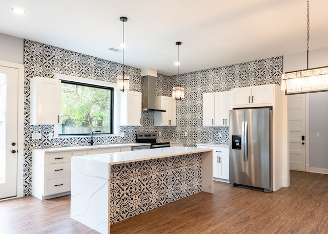 kitchen featuring hanging light fixtures, a kitchen island, stainless steel appliances, and wall chimney range hood