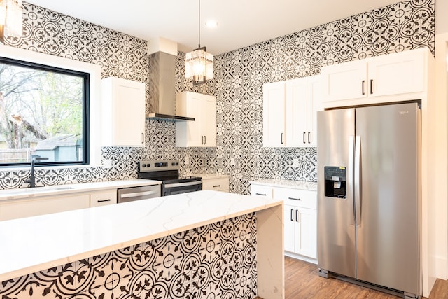 kitchen featuring wall chimney exhaust hood, stainless steel appliances, light stone counters, decorative light fixtures, and white cabinets