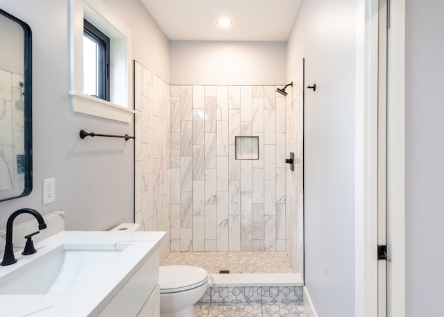 bathroom with tile patterned flooring, a tile shower, vanity, and toilet