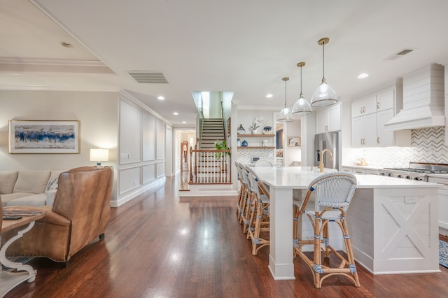 kitchen featuring pendant lighting, custom exhaust hood, a center island with sink, white cabinets, and a kitchen bar