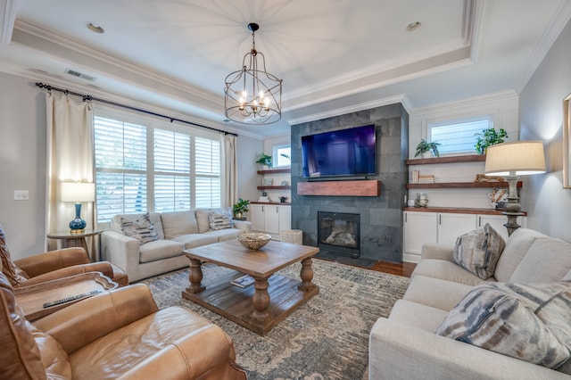 living room featuring hardwood / wood-style floors, a raised ceiling, crown molding, a fireplace, and a notable chandelier