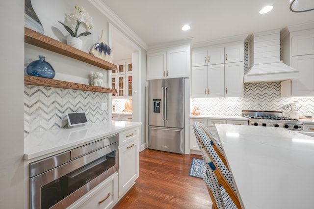 kitchen featuring dark hardwood / wood-style flooring, backsplash, white cabinets, custom range hood, and appliances with stainless steel finishes