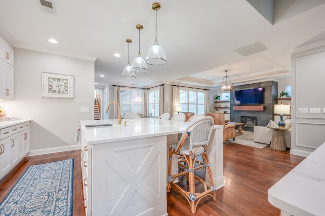 kitchen with a kitchen bar, light stone countertops, white cabinets, dark hardwood / wood-style floors, and an island with sink