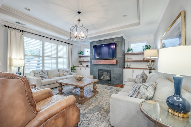 living room featuring a tiled fireplace, a chandelier, and ornamental molding