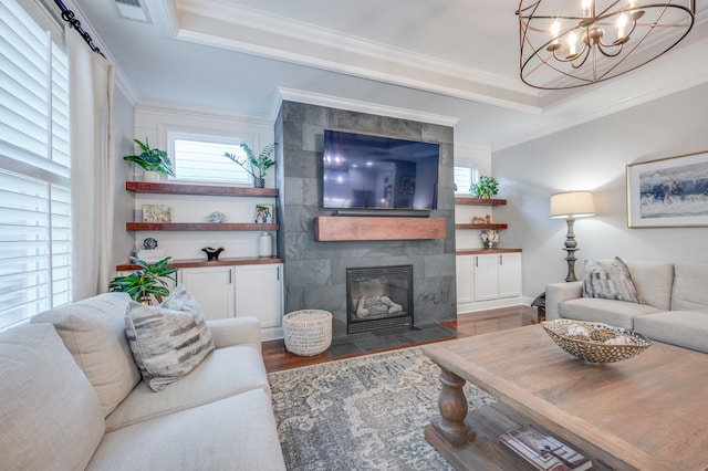 living room with a tray ceiling, a tile fireplace, hardwood / wood-style floors, and ornamental molding