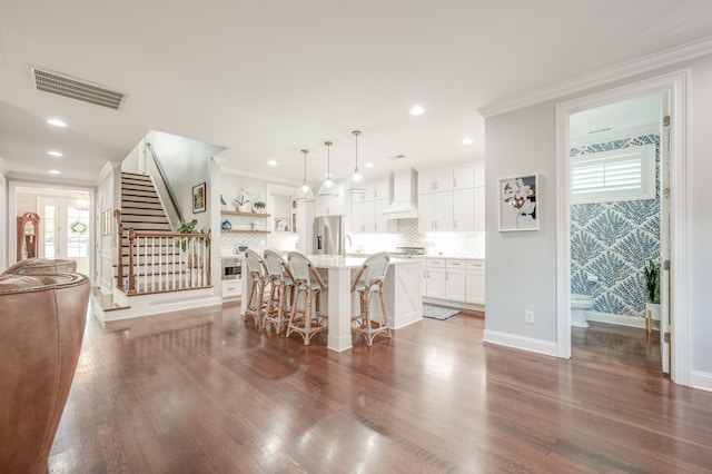 kitchen featuring a kitchen breakfast bar, premium range hood, a kitchen island with sink, pendant lighting, and stainless steel fridge with ice dispenser