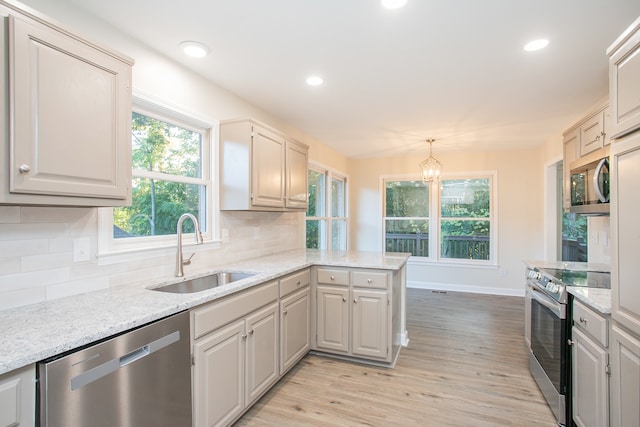 kitchen with pendant lighting, light wood-type flooring, appliances with stainless steel finishes, tasteful backsplash, and kitchen peninsula