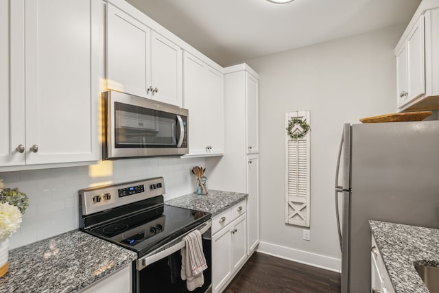 kitchen featuring white cabinets, decorative backsplash, stainless steel appliances, and dark stone countertops