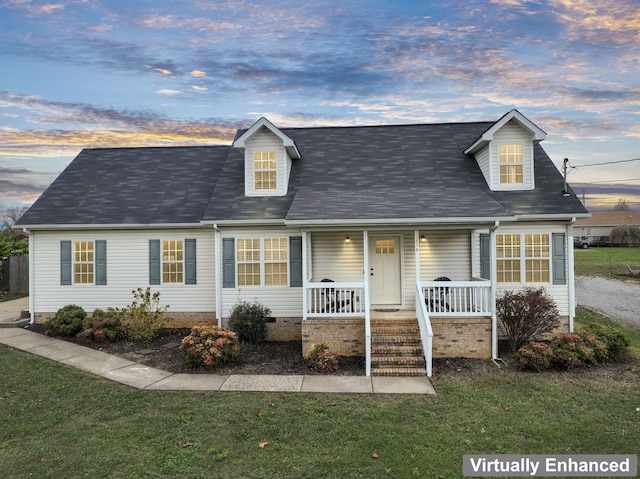 cape cod-style house with a lawn and covered porch