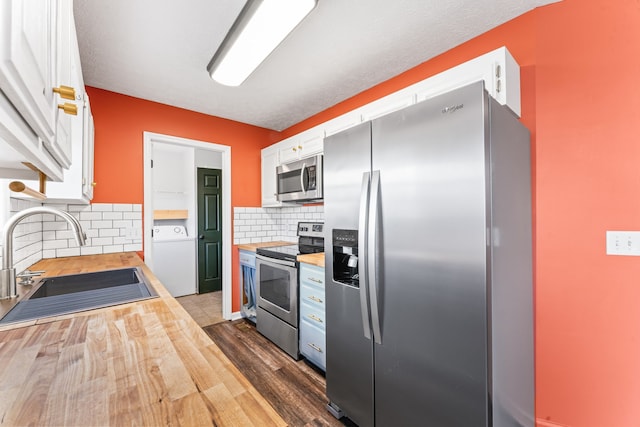 kitchen with dark wood-type flooring, sink, appliances with stainless steel finishes, white cabinetry, and washer / clothes dryer