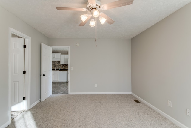 unfurnished room with ceiling fan, light colored carpet, and a textured ceiling