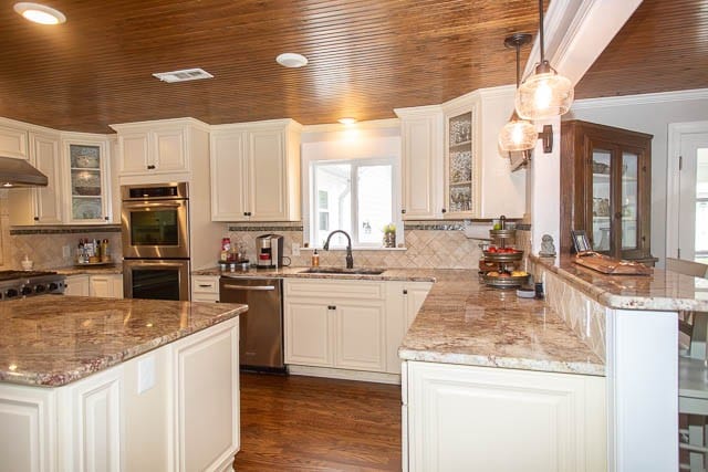 kitchen featuring pendant lighting, sink, decorative backsplash, white cabinetry, and stainless steel appliances