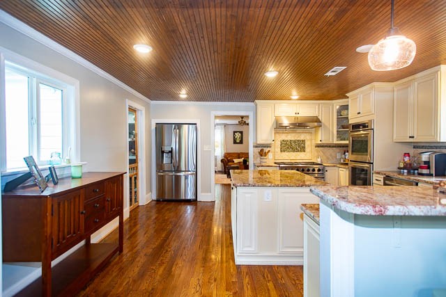 kitchen with stainless steel appliances, crown molding, pendant lighting, dark hardwood / wood-style floors, and white cabinetry