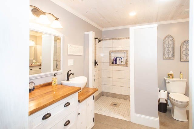 bathroom with vanity, tile patterned floors, crown molding, toilet, and tiled shower