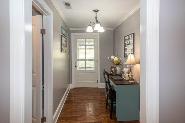 doorway with dark hardwood / wood-style floors, an inviting chandelier, and crown molding