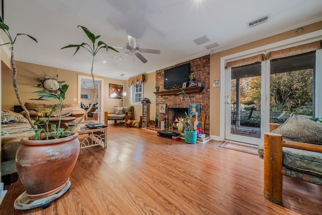 living room with hardwood / wood-style floors, ceiling fan, crown molding, and a brick fireplace