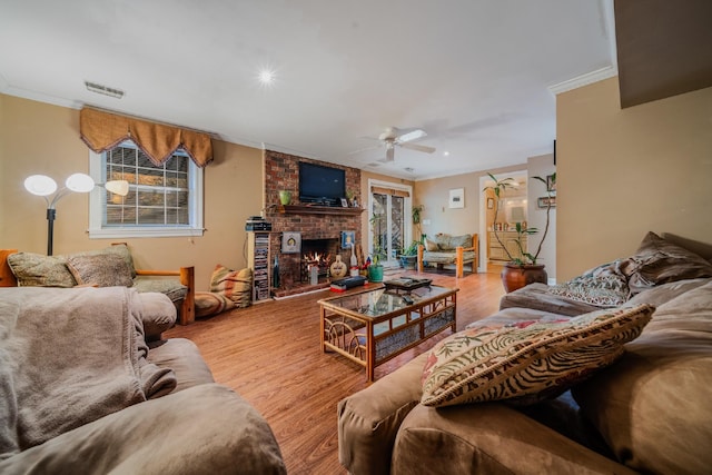 living room with a fireplace, light hardwood / wood-style floors, ceiling fan, and crown molding