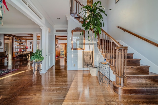 foyer entrance featuring hardwood / wood-style flooring, crown molding, and decorative columns