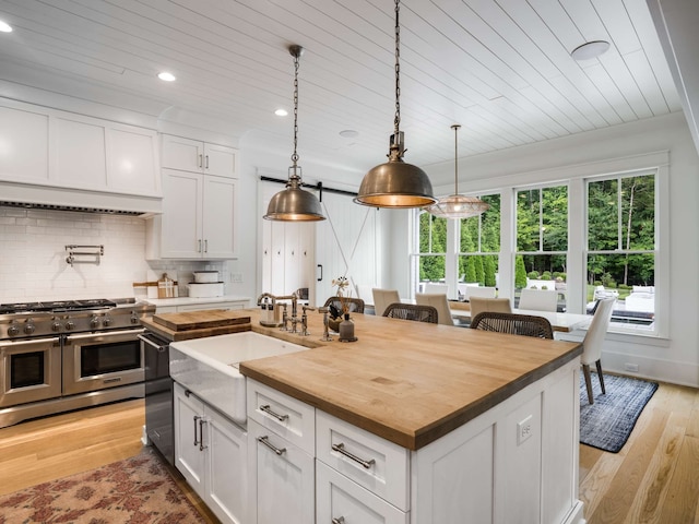 kitchen with pendant lighting, white cabinetry, stainless steel appliances, and a kitchen island with sink