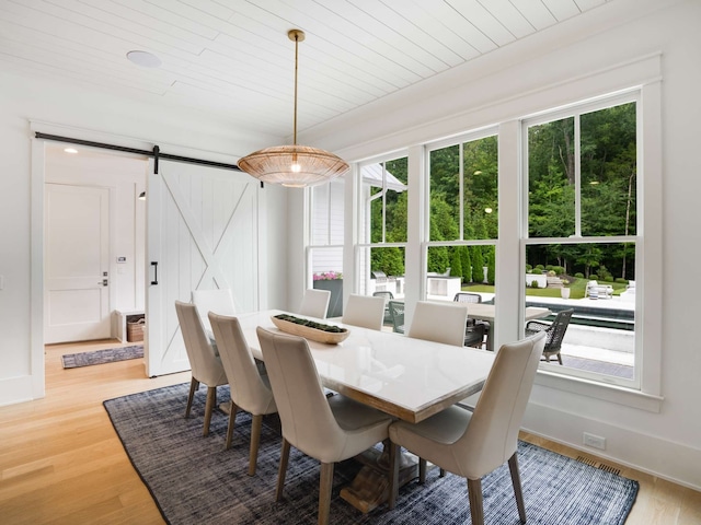 dining space featuring a barn door, wood-type flooring, and a wealth of natural light