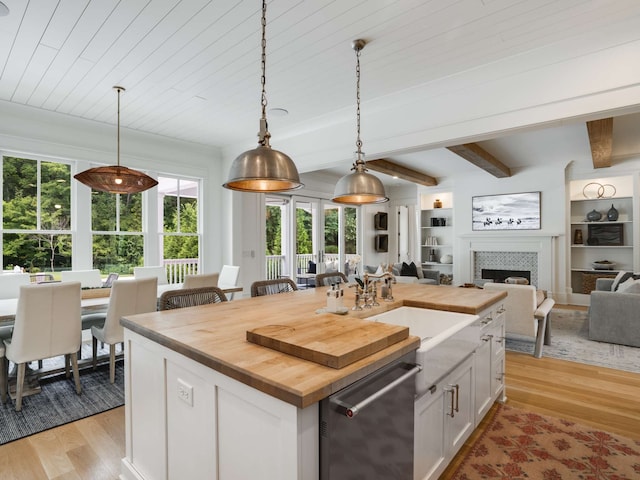 kitchen with dishwasher, hanging light fixtures, light hardwood / wood-style floors, a center island with sink, and white cabinets