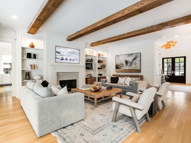 living room with beamed ceiling, french doors, light wood-type flooring, and a tile fireplace