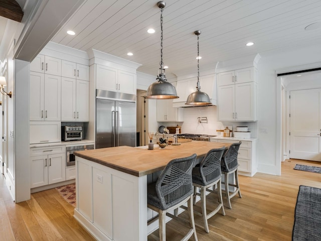 kitchen with butcher block countertops, white cabinetry, a kitchen island with sink, and appliances with stainless steel finishes