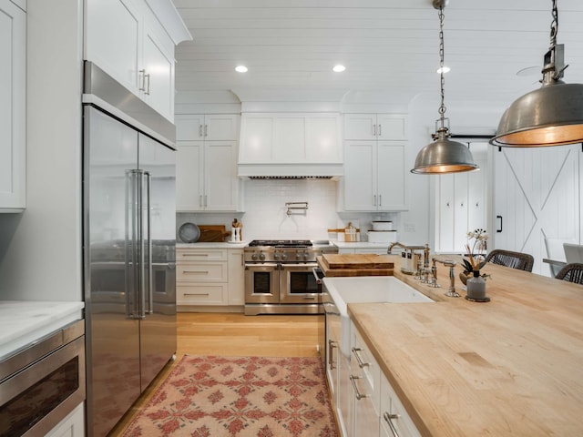 kitchen featuring wooden counters, hanging light fixtures, light hardwood / wood-style flooring, premium appliances, and white cabinetry