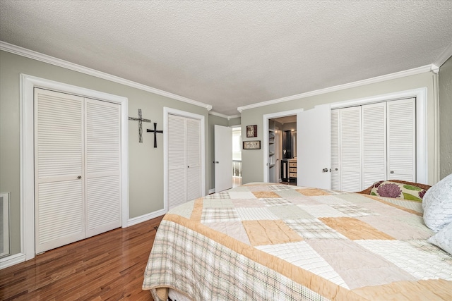 bedroom featuring a textured ceiling, ornamental molding, wood-type flooring, and multiple closets