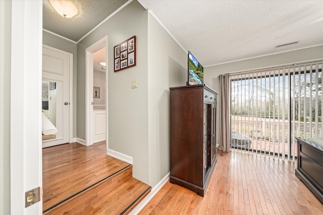 hallway featuring a textured ceiling, light hardwood / wood-style floors, and crown molding